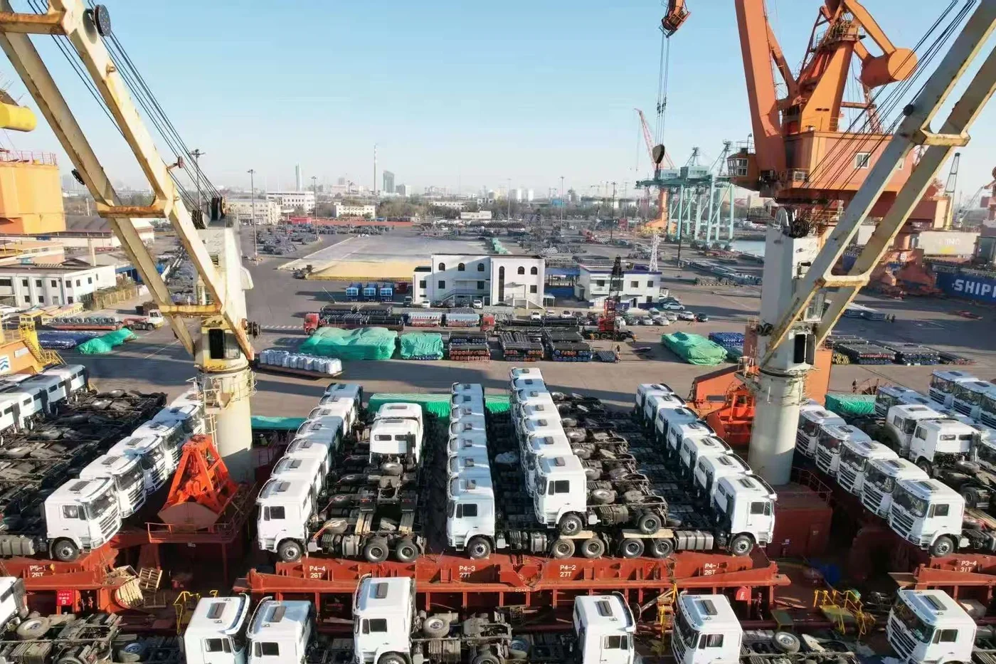 Trucks being lifted by ship crane at the port, with a vessel loaded with more units
